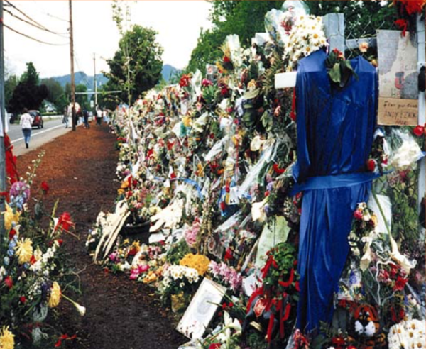 Image of the Thurston shooting memorial, 1998, Oregon. Several floral wreaths are displayed alongside the school grounds. Image Credits: United State’s Attorney’s Office, District of Minnesota (Wikimedia Commons).
